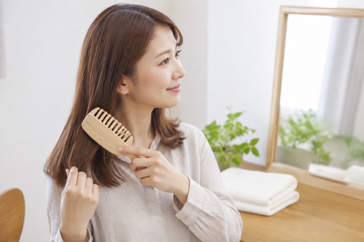 洗髪前に乾いた髪の毛先から木製の目の粗いブラシでやさしくとかす女性